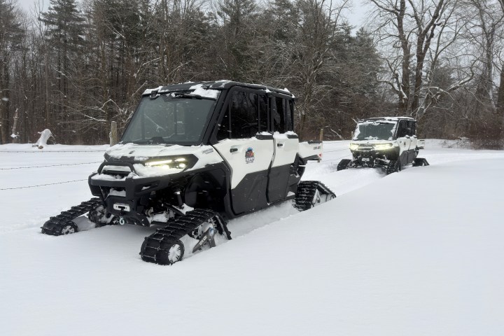 Two snow track vehicles driving through a snowy forest area.