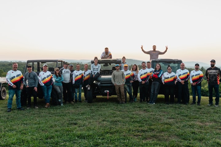 Group of people in matching jerseys posing with off-road vehicles on a grassy hillside.